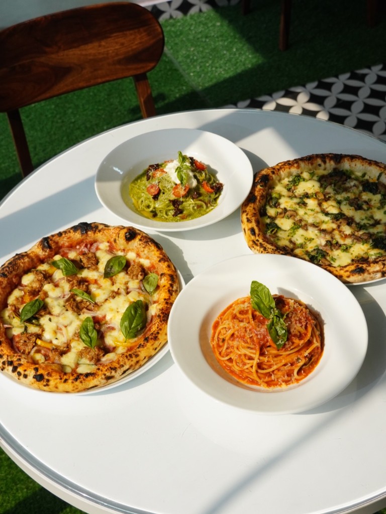 Neapolitan pizzas and pesto and pomodoro pasta bowls on a white table at Naples in a Box